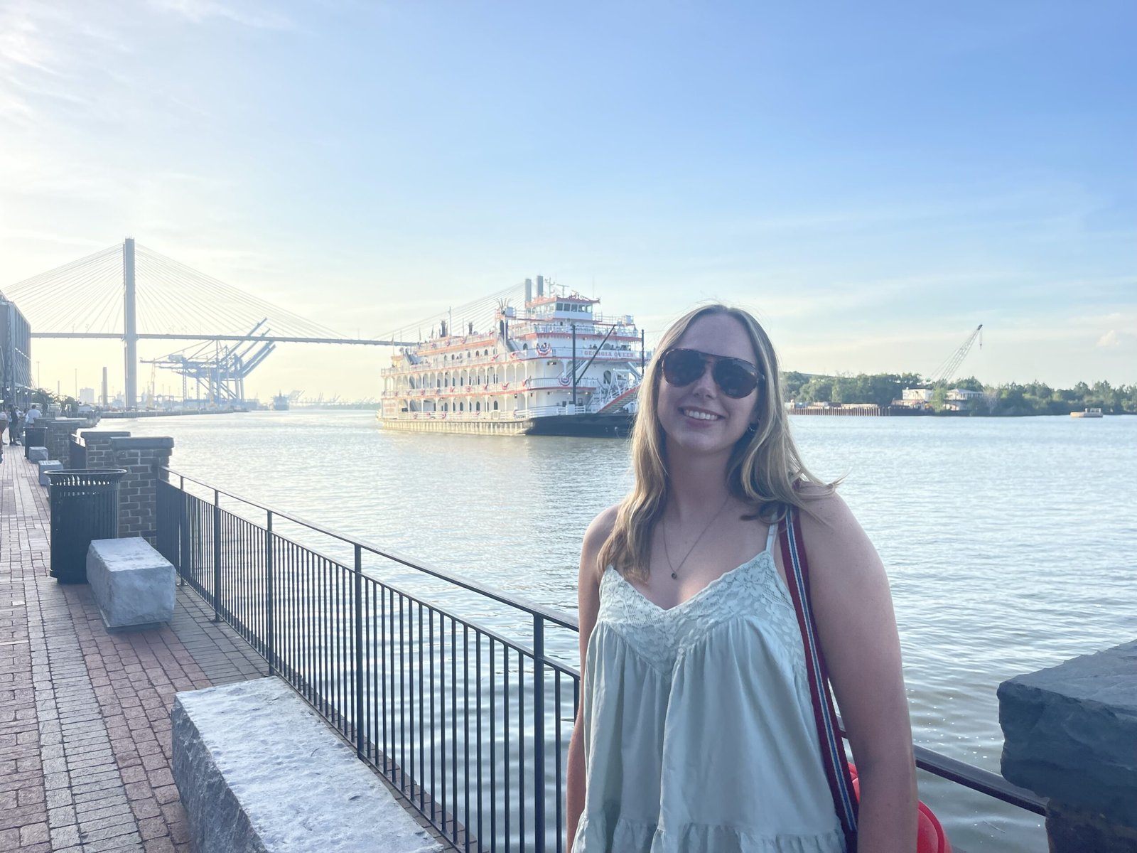 Woman smiling on the Savannah riverfront with the Georgia Queen riverboat in the background